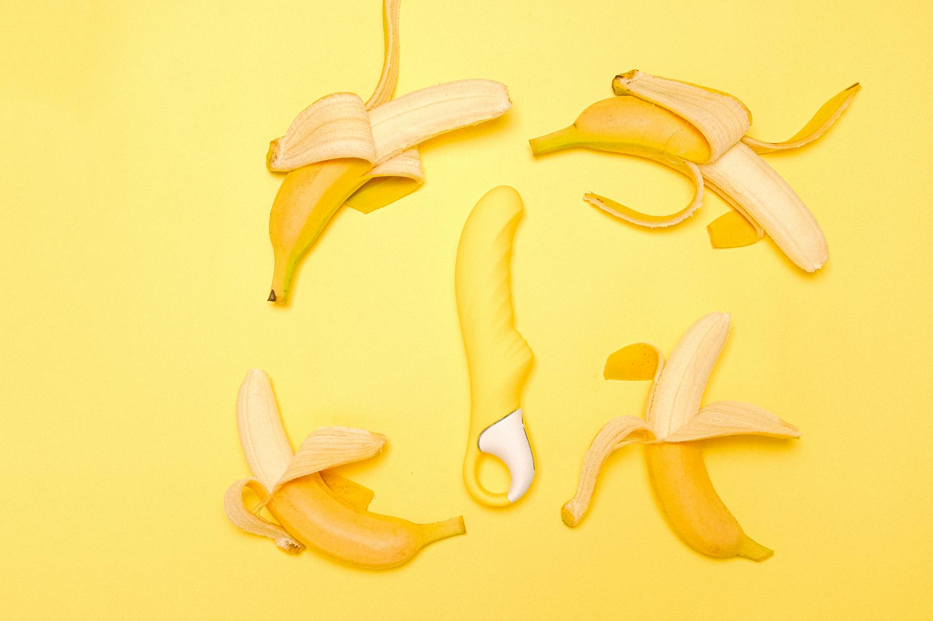 Yellow silicone lemon vibrator surrounded by fresh peeled lemons on bright yellow background