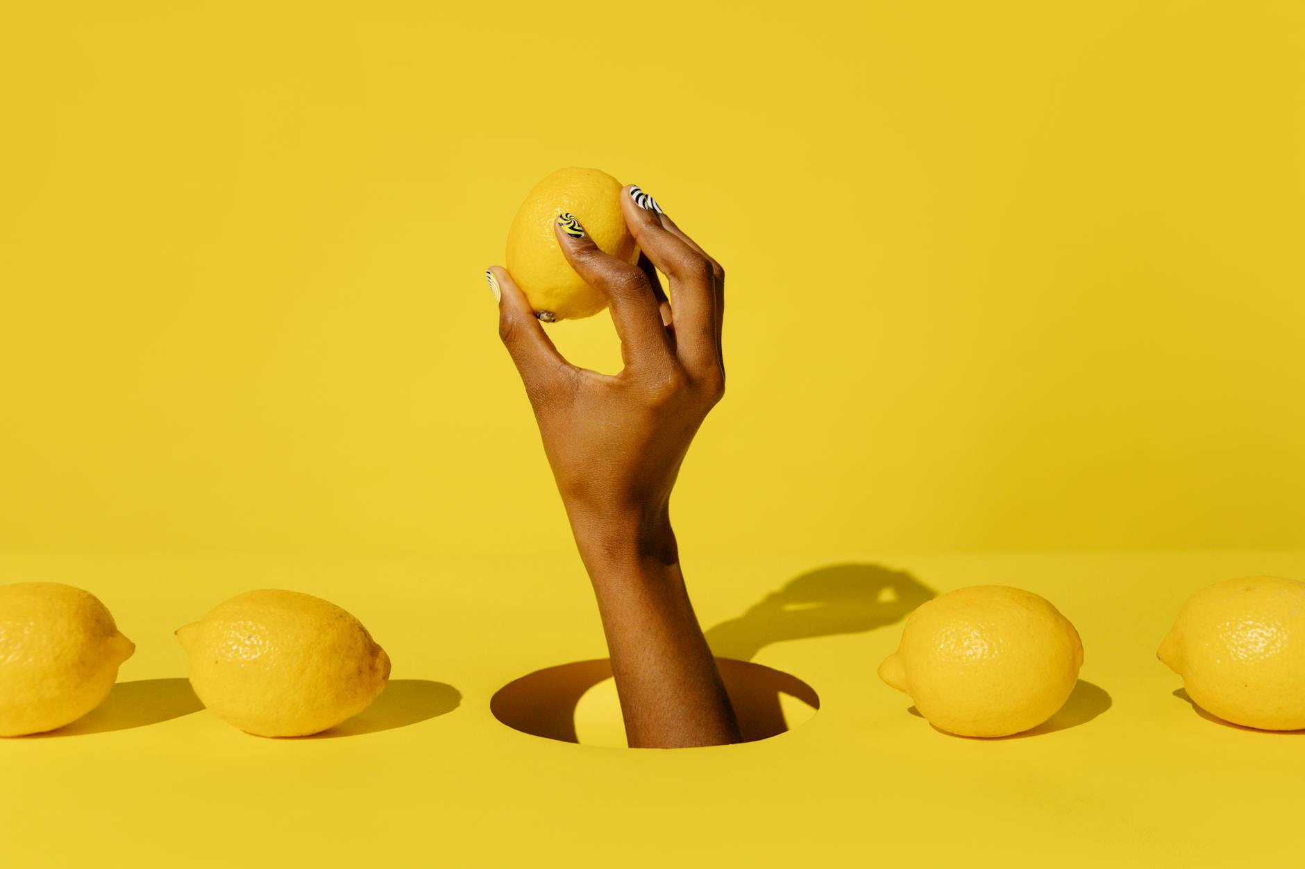 A hand holding a lemon against a vivid yellow background, symbolizing freshness and new beginnings during emotional healing.