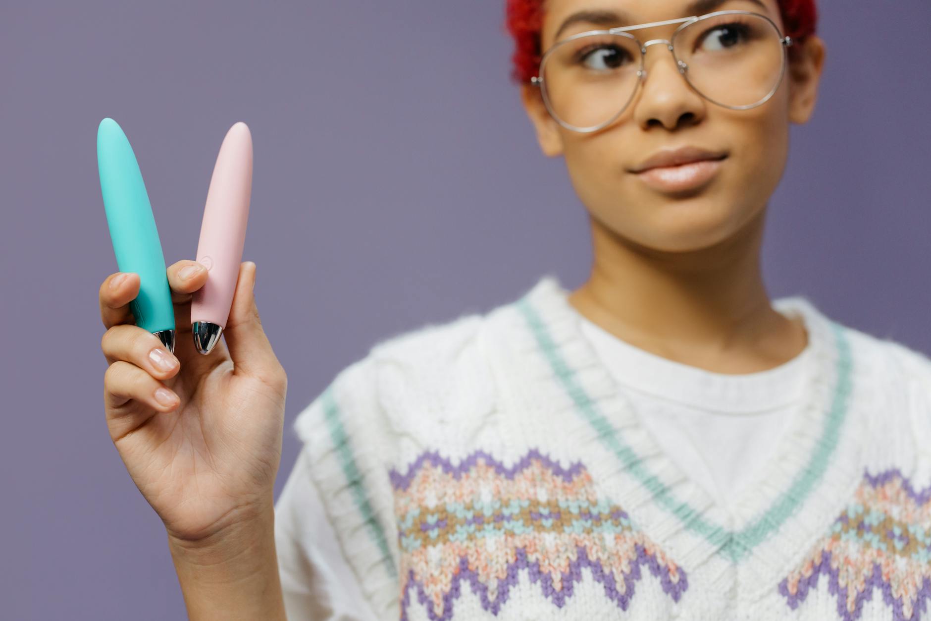 Woman with eyeglasses holding colorful silicone vibrators in a contemplative manner.