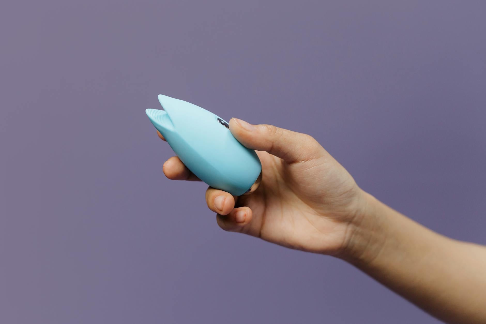 Woman holding blue and pink silicone vibrators in contemplative posture