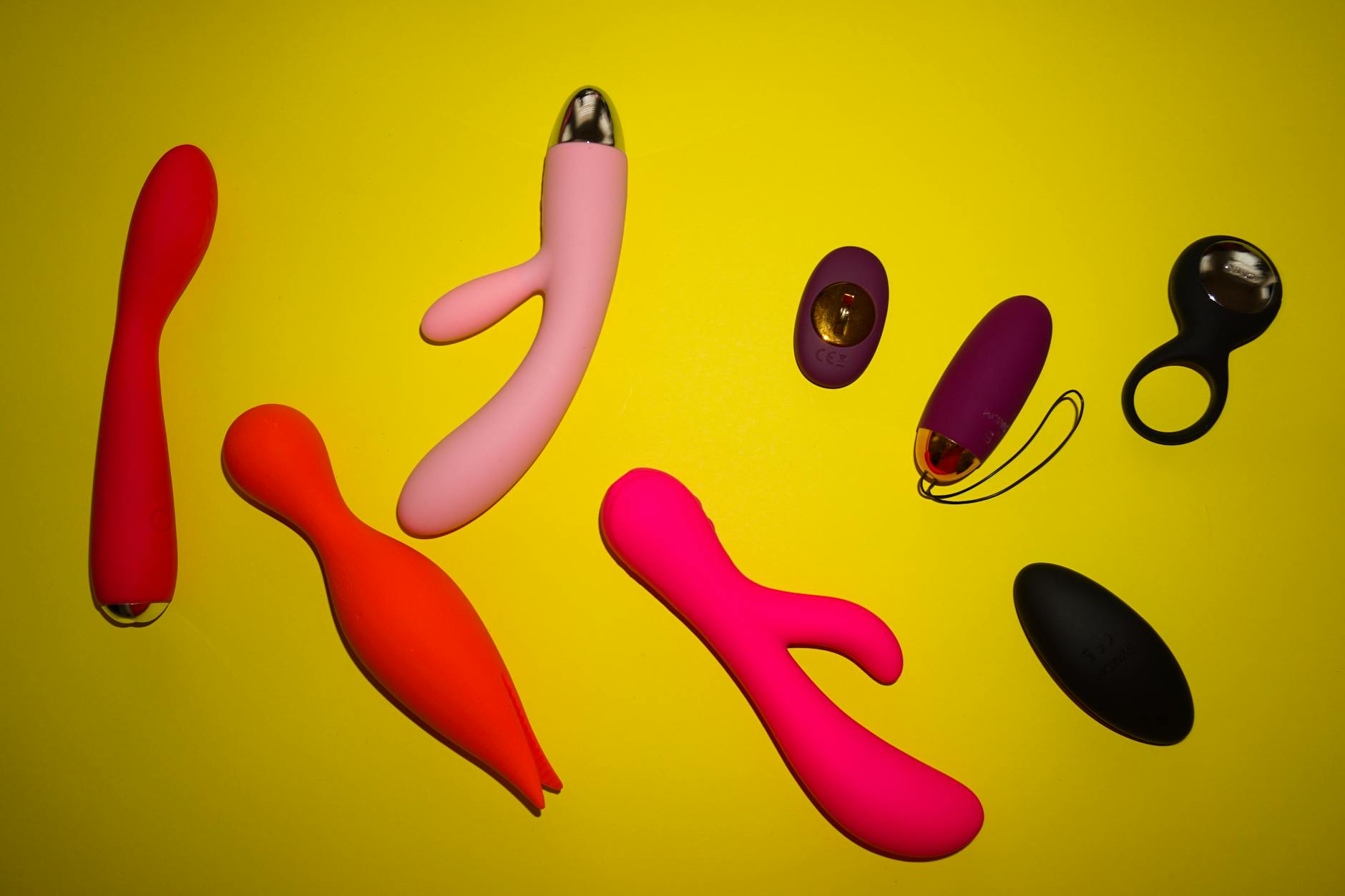 Colorful adult toys arranged on a bright yellow surface, showcasing variety in clitoral vibrator designs